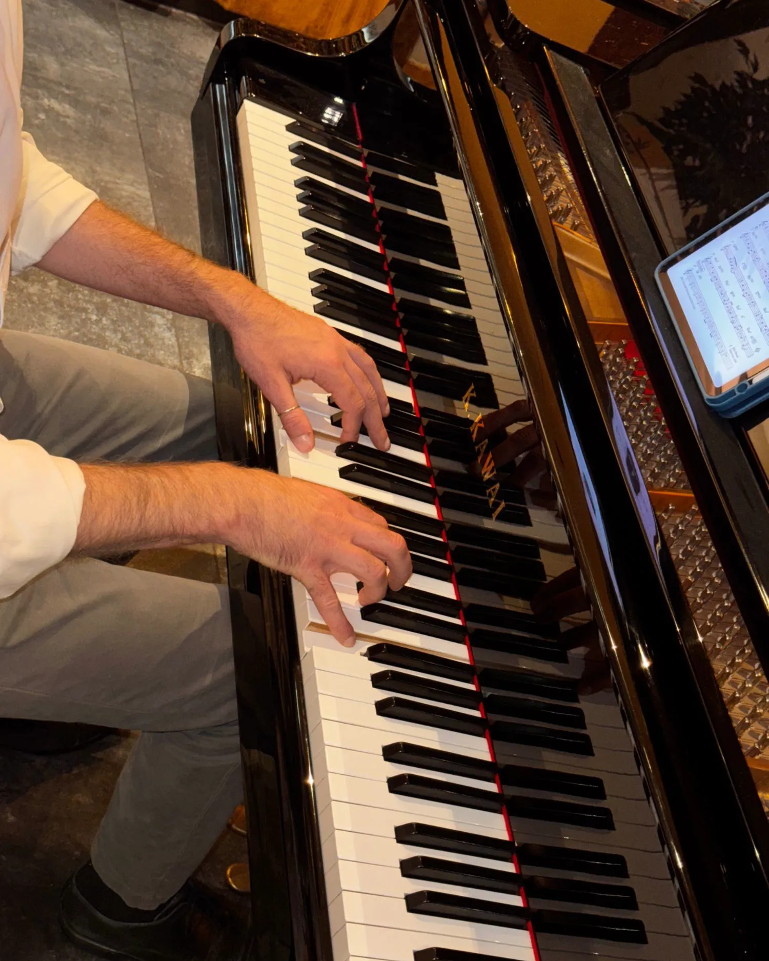 Hände auf den Tasten eines Kawai-Flügels, Noten auf dem Tablet